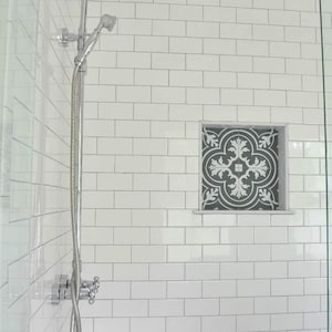 May include: A white tiled shower with a chrome shower head and a decorative tile inset. The shower has a chrome shower arm and a handheld shower head.