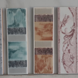 Puede incluir: Cinco muestras de azulejos de cerámica con diferentes diseños. Los azulejos son rectangulares y tienen un fondo blanco. Los diseños incluyen un patrón floral, un patrón geométrico, un patrón de acuarela y un patrón floral con un tono rosado. Los azulejos están dispuestos en una fila de izquierda a derecha.