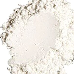 May include: A close-up of a white powder, likely a cosmetic product like face powder or setting powder. The powder is in a pile, with a slightly rough texture.