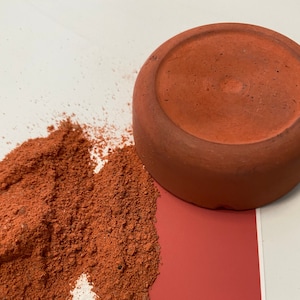 May include: A terracotta pot with a red powder spilling out of it. The powder is on a white surface and a red surface.