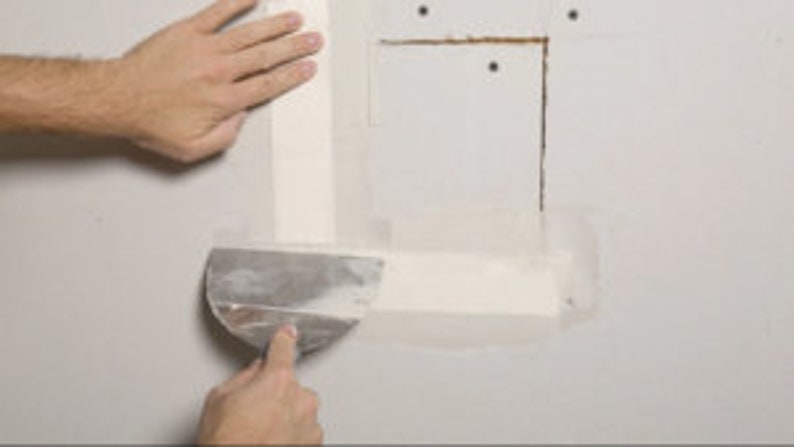 May include: A person using a putty knife to apply joint compound to a wall, covering a hole with drywall tape.