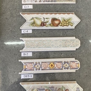 Op de afbeelding: Vijf verschillende tegelrandontwerpen met verschillende patronen en kleuren. De ontwerpen omvatten een bloemenpatroon, een fruitpatroon en een geometrisch patroon. De tegelranden zijn gelabeld met de volgende codes: G-3, C-4, B-2, DFP-9 en WH-1.