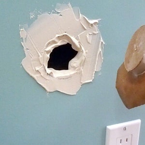 May include: A close-up of a wall with a hole patched with drywall compound. A drywall patch tool is shown separately.