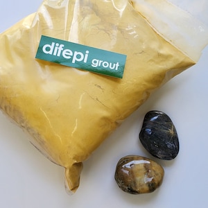 May include: A bag of yellow grout powder with a green label that says "dife pi grout" and two smooth stones, one black and one brown.