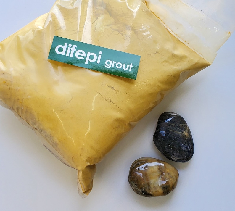 May include: A bag of yellow grout powder with a green label that says "dife pi grout" and two smooth stones, one black and one brown.