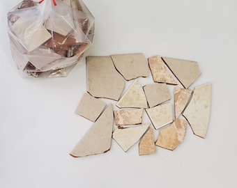 May include: A bag of broken beige and brown ceramic tiles. The tiles are in various shapes and sizes.