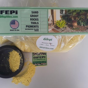 May include: A bag of yellow decorative filler powder labeled "difepi Decorative Filler Sand - Stone - Grout" with the website difepitiles.com. The bag is sitting on a white surface with a small black bowl containing the same yellow powder.