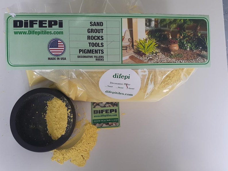 May include: A bag of yellow decorative filler powder labeled "difepi Decorative Filler Sand - Stone - Grout" with the website difepitiles.com. The bag is sitting on a white surface with a small black bowl containing the same yellow powder.