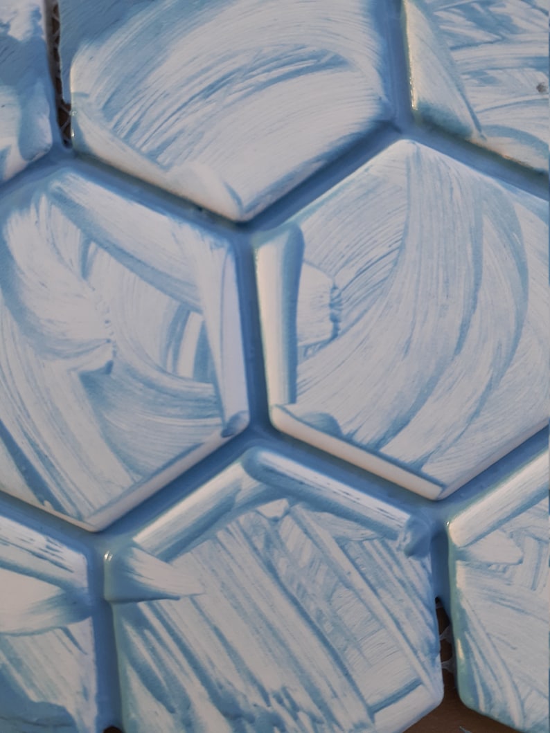 May include: Close-up of a wall covered in white and light blue hexagonal tiles. The tiles have a textured, brushed finish.