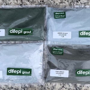 Könnte beinhalten: Vier Beutel ungesiebter Fugenmörtel in verschiedenen Grüntönen. Die Beutel sind mit dem Namen "difepi grout" sowie der Farbe und dem Gewicht des Fugenmörtels beschriftet. Die Beutel befinden sich auf einer hellgrauen Oberfläche.