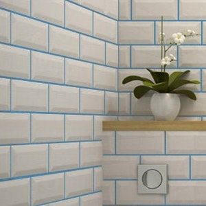 May include: White subway tile with blue grout lines. The tiles are arranged in a brick pattern. A small wooden shelf is mounted on the wall, with a white ceramic planter holding a green plant with white flowers.