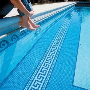 May include: A blue swimming pool with a white and blue mosaic tile border. The pool has a light blue liner and a white concrete deck.