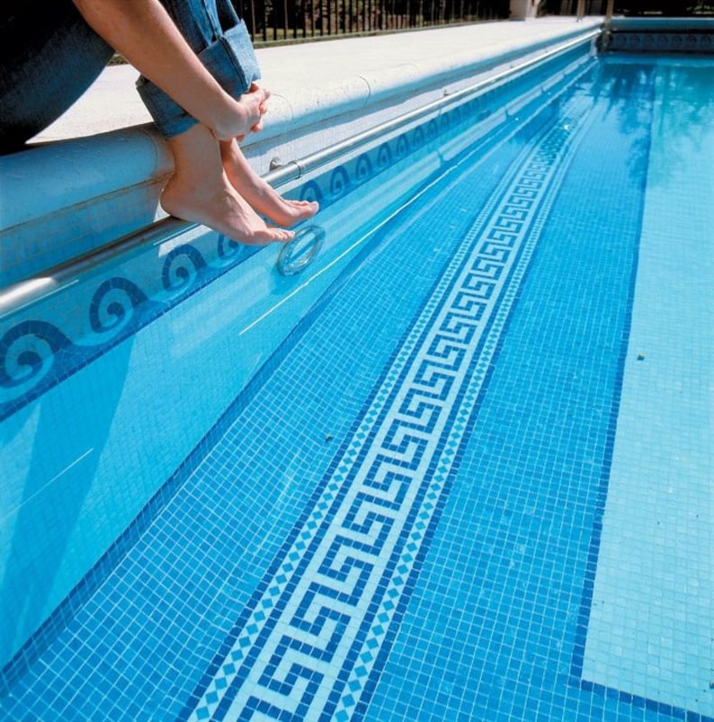 May include: A blue swimming pool with a white and blue mosaic tile border. The pool has a light blue liner and a white concrete deck.
