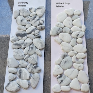 May include: Two samples of decorative pebbles, one in dark grey and one in white and grey. The samples are arranged in a vertical line, with the dark grey pebbles on the left and the white and grey pebbles on the right. The samples are labelled "Dark Grey Pebbles" and "White & Grey Pebbles".