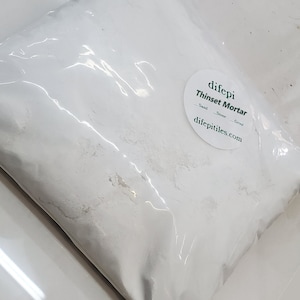 Puede incluir: Una bolsa de plástico blanca llena de polvo blanco con la etiqueta "difepi Thinset Mortar" y el sitio web "difepetiles.com".