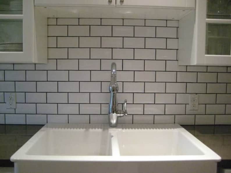 May include: A white porcelain kitchen sink with two basins and a chrome faucet. The sink is installed in a countertop with white metro tiles as a backsplash.