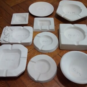 May include: A collection of white ceramic bowls and dishes of various sizes and shapes. The bowls and dishes have handwritten measurements in inches on the bottom.