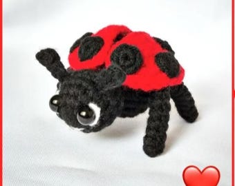 Puede incluir: Un juguete de mariquita de crochet con patas negras y una cáscara roja con manchas negras. La mariquita tiene grandes ojos negros con pupilas blancas.