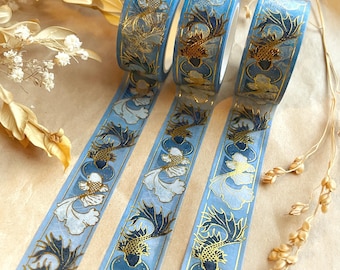 May include: Three rolls of decorative washi tape with a blue background and a repeating pattern of gold and navy koi fish and white floral accents. The tape is partially unrolled, revealing the design.