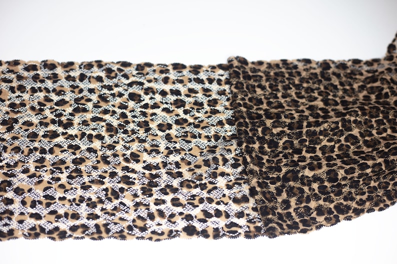 May include: A close-up of a brown and black leopard print fabric with a glittery finish. The fabric is folded in half, showing both sides.