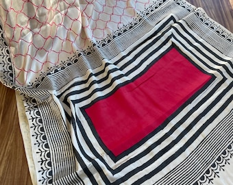 May include: A white cotton saree with a black and white striped border and a red inner square. The saree has a delicate white and pink floral pattern.