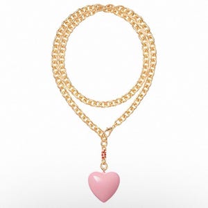 May include: Gold-tone chain necklace with a pink heart pendant. The necklace features a double-strand chain design and a lobster clasp closure. The heart pendant is a soft pink color and adds a touch of romance to the necklace.