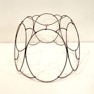 May include: A dark metal wire wine rack with an open, circular design. The rack features multiple oval openings and a small, gold-colored accent in the center. The overall shape is cylindrical, suitable for holding wine bottles.