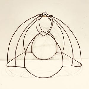 May include: A dark brown metal lampshade frame with a series of curved and circular wire elements. The frame has a rounded shape, with a small, decorative piece at the top. The design is open and airy.