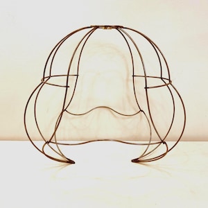 Puede incluir: Un marco de pantalla de lámpara de metal marrón con un diseño redondeado en forma de jaula. El marco está hecho de finas varillas de metal que se curvan y se cruzan para formar la forma. El marco de la pantalla de la lámpara está diseñado para sostener una bombilla y difundir la luz.