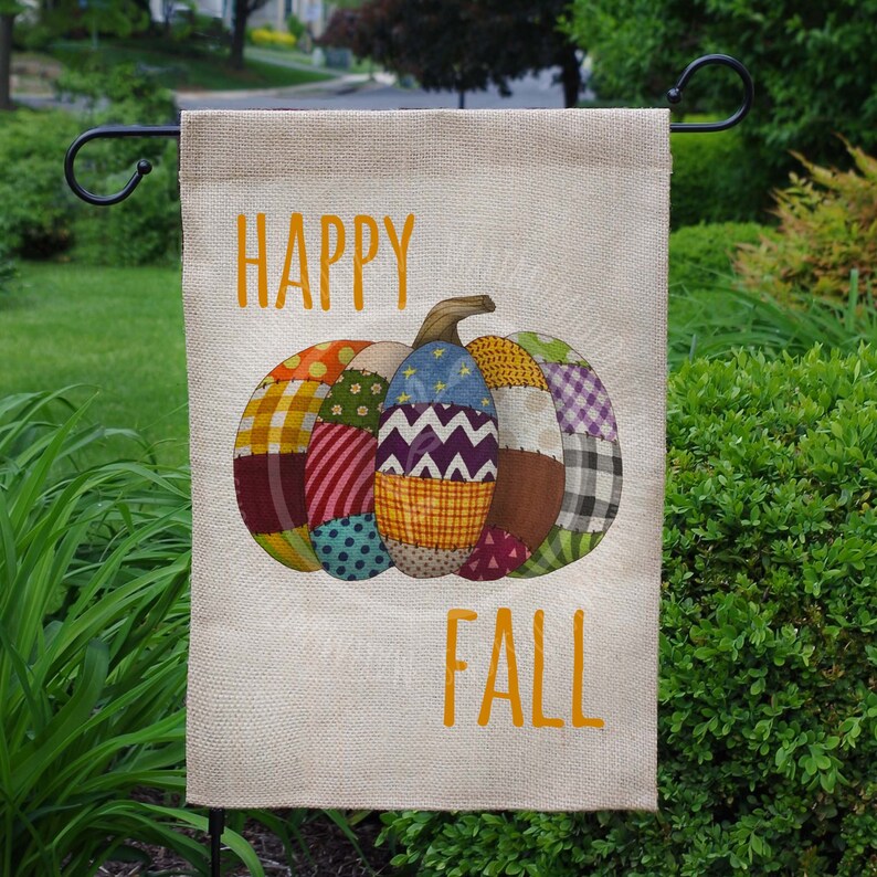 K&ouml;nnte beinhalten: Eine Gartenflagge aus Sackleinen mit dem Text "Happy Fall" in orangefarbenen Buchstaben. In der Mitte der Flagge befindet sich ein bunter Patchwork-K&uuml;rbis.