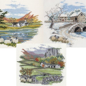 May include: Three cross-stitch landscape pictures. One shows a lake with sheep, a tree, and mountains. Another depicts a snow-covered bridge and buildings. The third features a stone bridge and autumn foliage.