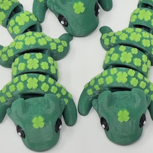 Op de afbeelding: Groene beweegbare slangenspeelgoed met lichtgroene klaveraccenten. De slang heeft zwarte ogen en is gemaakt van plastic. Een leuk en uniek item voor kinderen en verzamelaars.