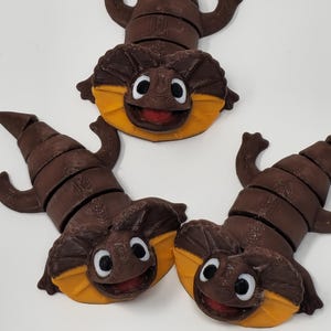 May include: Several brown lizard-like figurines with yellow and red accents. Each has a smiling face with white eyes. The figurines are arranged on a white surface.