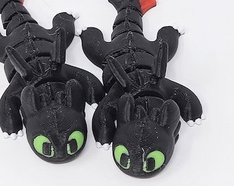 Puede incluir: Dos figuras de dragón negras con ojos verdes y detalles rojos y blancos. Las figuras están sobre una superficie blanca. Los dragones tienen un diseño detallado y texturizado.