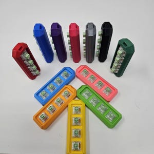 May include: A set of 12 colorful keycap holders, each with a different color and design. The holders are arranged in a circle, with a few in the center. The holders are made of plastic and have a smooth finish.