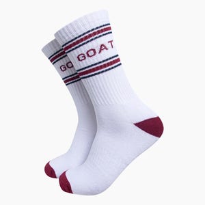 May include: A pair of white crew socks featuring ribbed cuffs with two horizontal dark blue stripes and one maroon stripe. The text GO GOAT is printed in maroon on the upper section. The toe and heel areas are accented with solid maroon fabric.