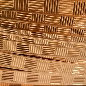 May include: Close-up of a roll of gold-colored metal trim with a checkered pattern. The trim is made of thin, flat metal and has a shiny finish.