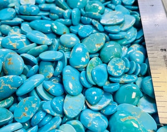Puede incluir: Una imagen de primer plano de un montón grande de cabujones de turquesa. Las piedras son de varios tonos de azul y verde, y algunas tienen un patrón veteado. Una regla es visible en el fondo.