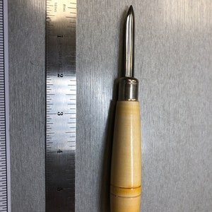 Peut inclure: Un outil en métal à manche en bois avec une pointe pointue. L'outil mesure environ 13 cm de long et a un manche en bois brun clair.