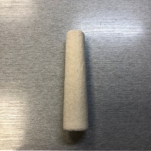 May include: A white felt cone-shaped polishing tool, approximately 2 inches long, shown on a silver surface with a ruler for scale.
