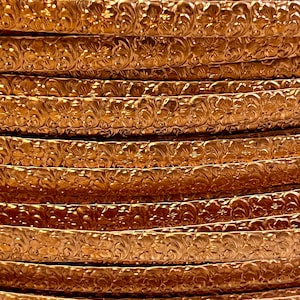 May include: Close-up of a stack of copper-colored metal trim with a floral embossed design.