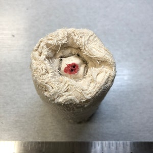 May include: A white fabric roll with a red circle in the center. The fabric is frayed and has a rough texture.