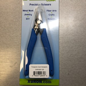 May include: Blue handled thread and cord scissors with a silver blade. The packaging says "Xuron Corp. Precision Scissors" and lists uses for metal work, jewelry, DIY, fiber arts, crafts, and hobbies. The product number is SHR-641.00.