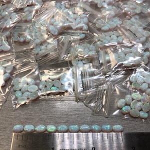 May include: A close-up of a ruler measuring a row of white oval-shaped opals. The opals are arranged in a line and are approximately 1 inch in length. The ruler is marked in inches and 16ths of an inch.