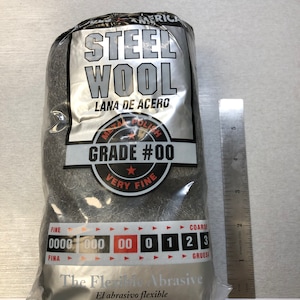 Könnte beinhalten: Eine Packung grauer Stahlwolle mit der Aufschrift "Steel Wool" und "Lana de Acero". Die Verpackung trägt außerdem die Aufschrift "Grade #00 Very Fine" und "The Flexible Abrasive".