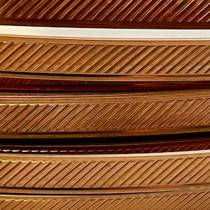 May include: Four stacked plates with a copper-coloured rim and a diagonal pattern. The plates are slightly curved.