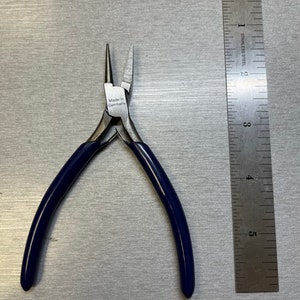 May include: Blue handled pliers with a silver finish and a label that reads "Made in Germany". The pliers are next to a ruler.