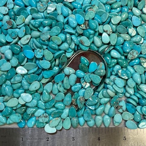 May include: A large collection of turquoise cabochons in a teardrop shape. The stones are a variety of shades of blue and green, and they are all polished to a smooth finish.