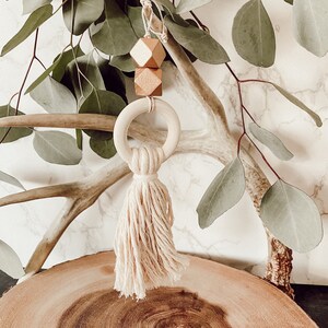 May include: A wooden ring with a knotted tassel hanging from it. The ring is decorated with two gold geometric shapes.