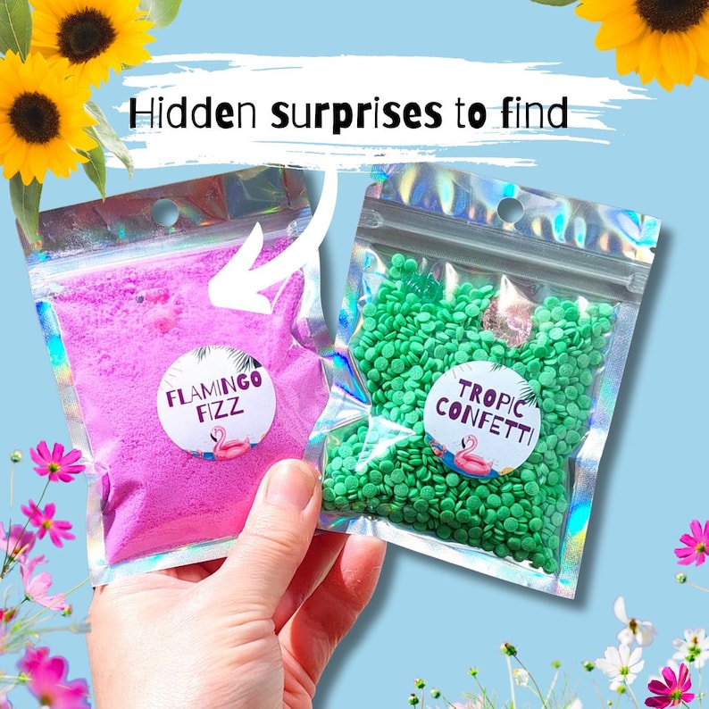 May include: Two clear, iridescent pouches filled with colorful contents. One contains pink powder labeled "Flamingo Fizz," the other green confetti labeled "Tropic Confetti." The text "Hidden surprises to find" is above the pouches. The background is light blue.
